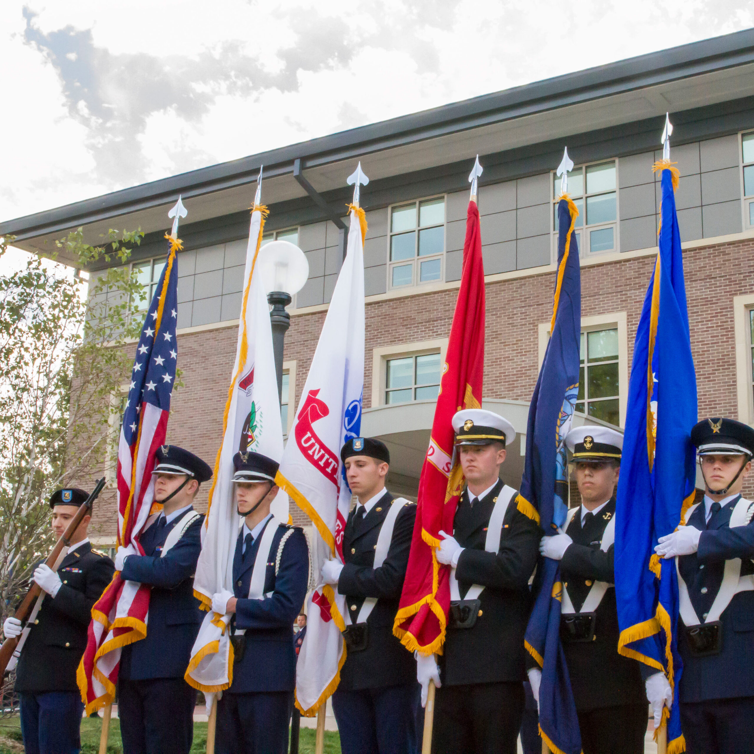 Men standing in front of the Chez Veteran's Center in uniform holding flags.