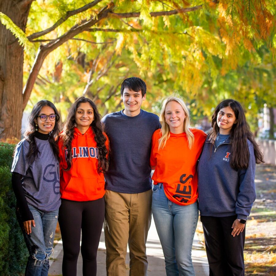 Students smiling and standing under the trees nearby the Business building.