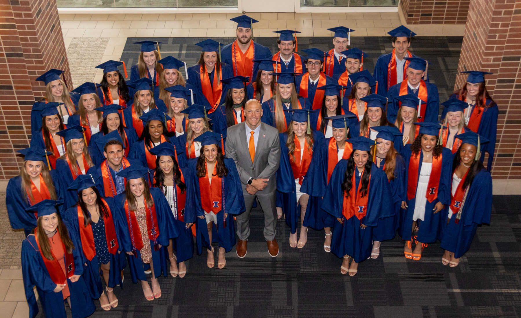 Josh Whitman and graduated Illinois women's athletes standing and smiling together.